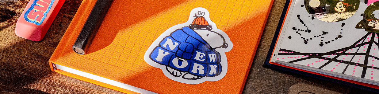 New York sticker on an orange notebook beside art supplies